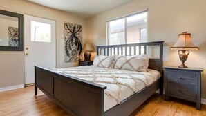Une chambre à coucher avec un lit, une table de chevet, une lampe, une fenêtre et une porte.