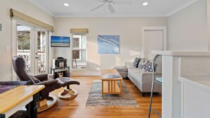 A spacious living room with a ceiling fan, a large window with a view, a sofa, a coffee table, and a fireplace. - 2 BR Cottage in 30A | Outdoor Pool, 2 Bikes | My Beach Getaways (Inlet Beach)