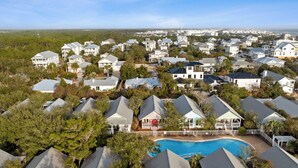 An aerial view of a residential area with houses, a swimming pool, and a distant view of a city skyline. - 2 BR Cottage in 30A | Outdoor Pool, 2 Bikes | My Beach Getaways (Inlet Beach)
