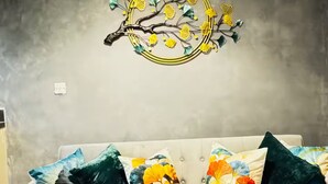 En grå sofa med puder i blomster- og løvdesign, billedkunst af en gren og en ensfarvet væg.