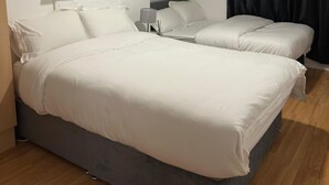 Slaapkamer met twee bedden, een nachtkastje, een lamp en een donker gordijn.