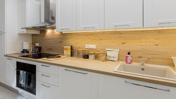 A modern kitchen with white cabinets, a wooden countertop, a built-in oven, and a stainless steel sink.