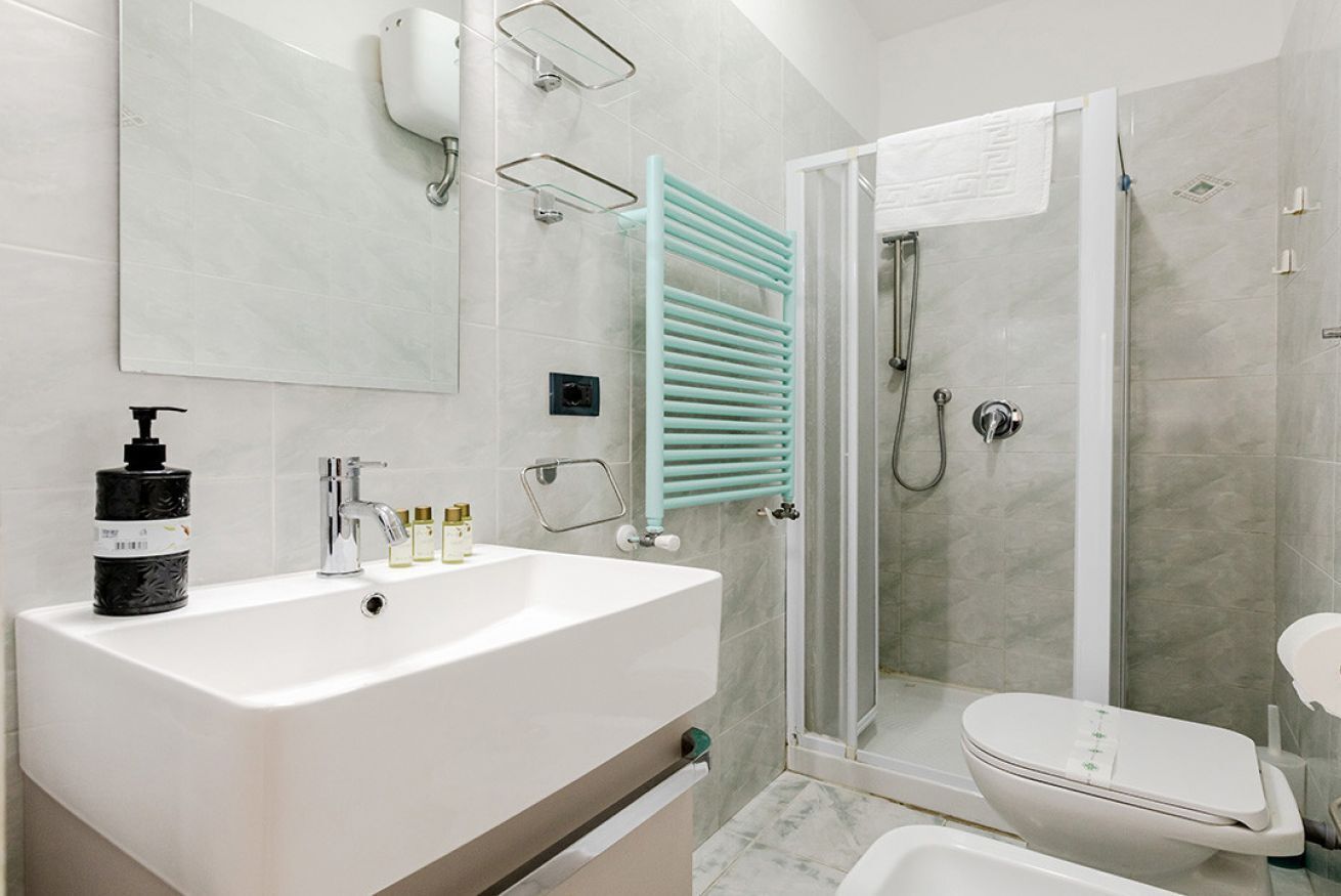 Un baño con lavamanos blanco, espejo, ducha con puerta de vidrio y retrete.
