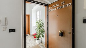 A hotel entrance with a wooden door labeled 'LA CASA DI NONNO ROBERTO,' a potted plant, and a telephone on the wall.