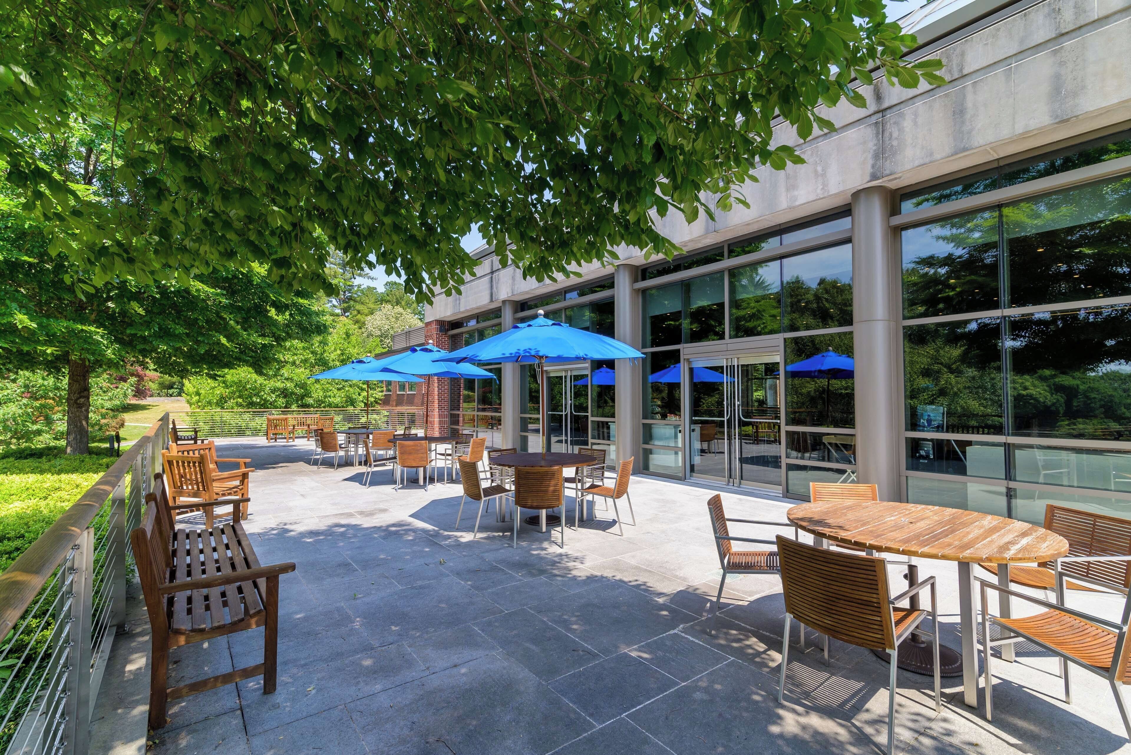 An outdoor patio with tables and chairs, blue umbrellas, and a glass building in the background.