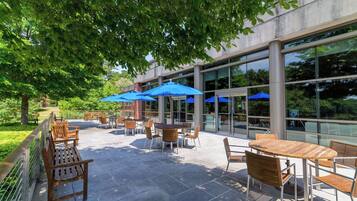 An outdoor patio with tables and chairs, blue umbrellas, and a glass building in the background.
