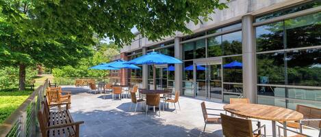 An outdoor patio with tables and chairs, blue umbrellas, and a glass building in the background.