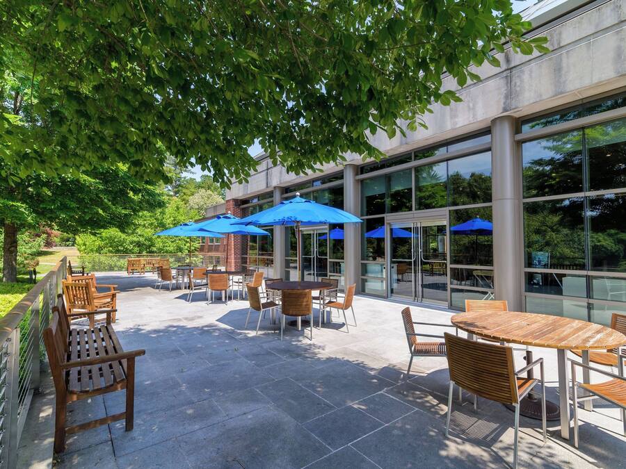 An outdoor patio with tables and chairs, blue umbrellas, and a glass building in the background.