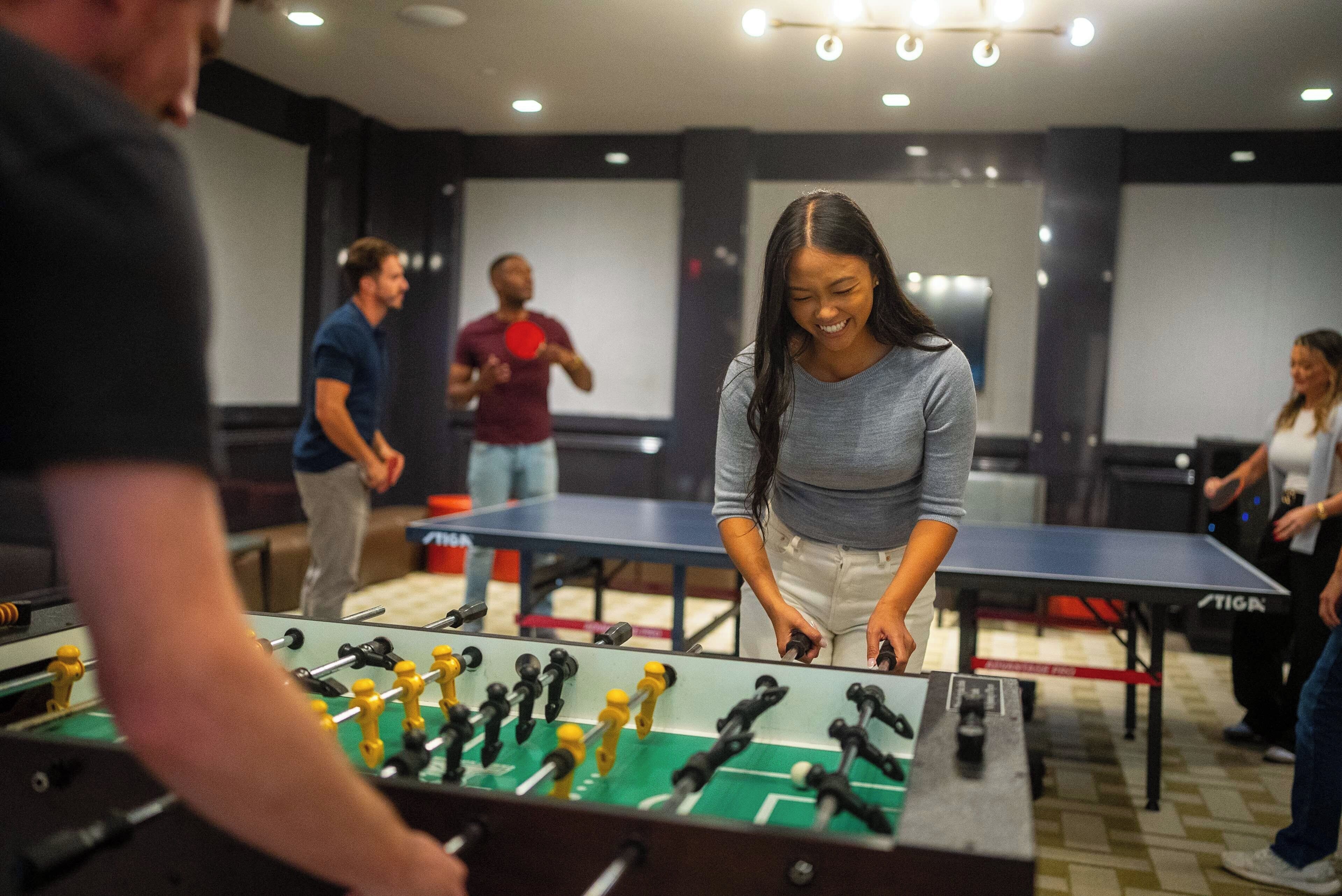 A room with multiple foosball tables and people playing.