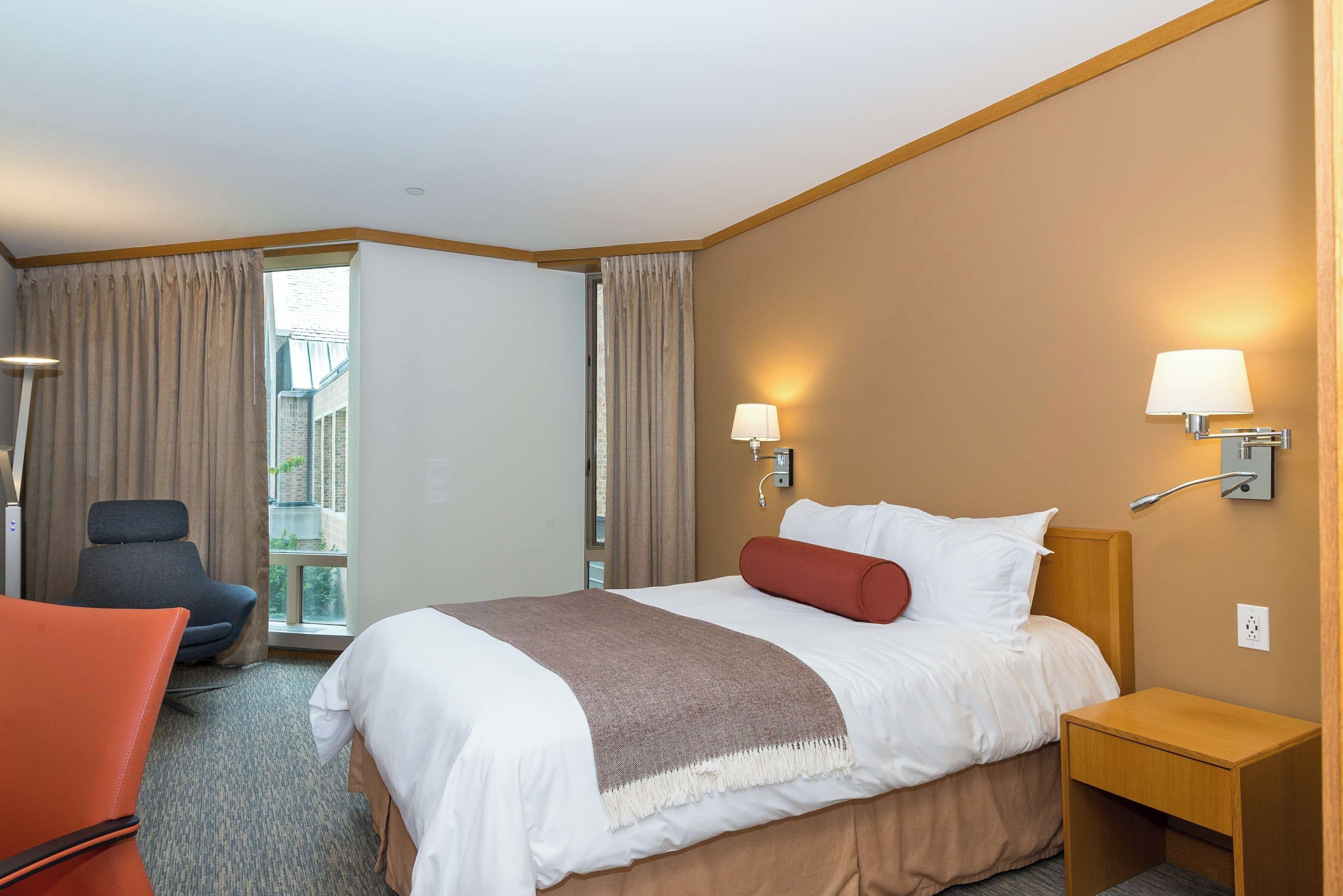 Et hotelværelse med seng, stol, natbord og lampe.