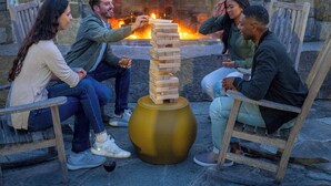 A stone fireplace with a fire, surrounded by outdoor seating. - Windrose On Hudson (Ossining)
