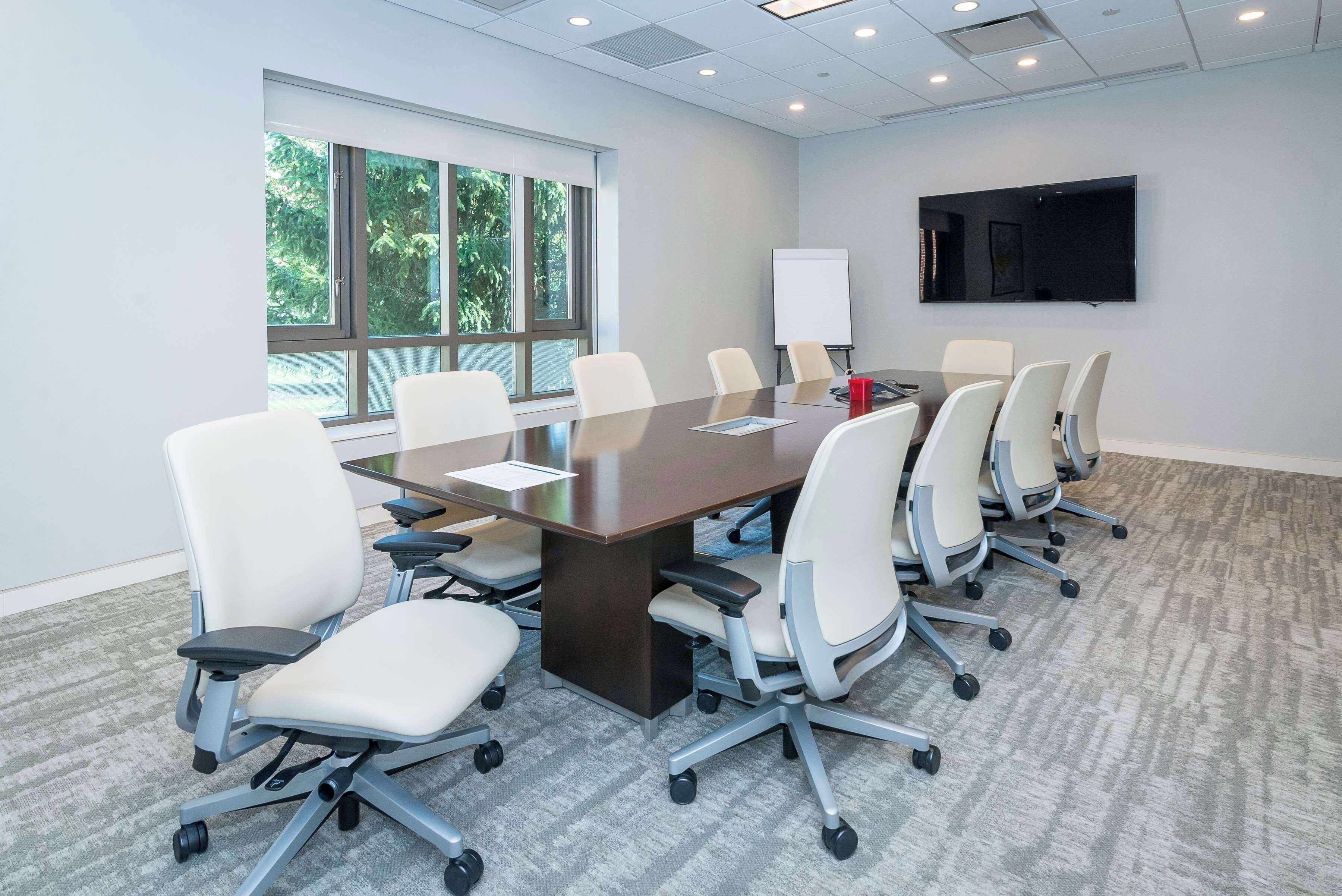 A conference room with a long table, multiple chairs, a whiteboard, and a TV screen.