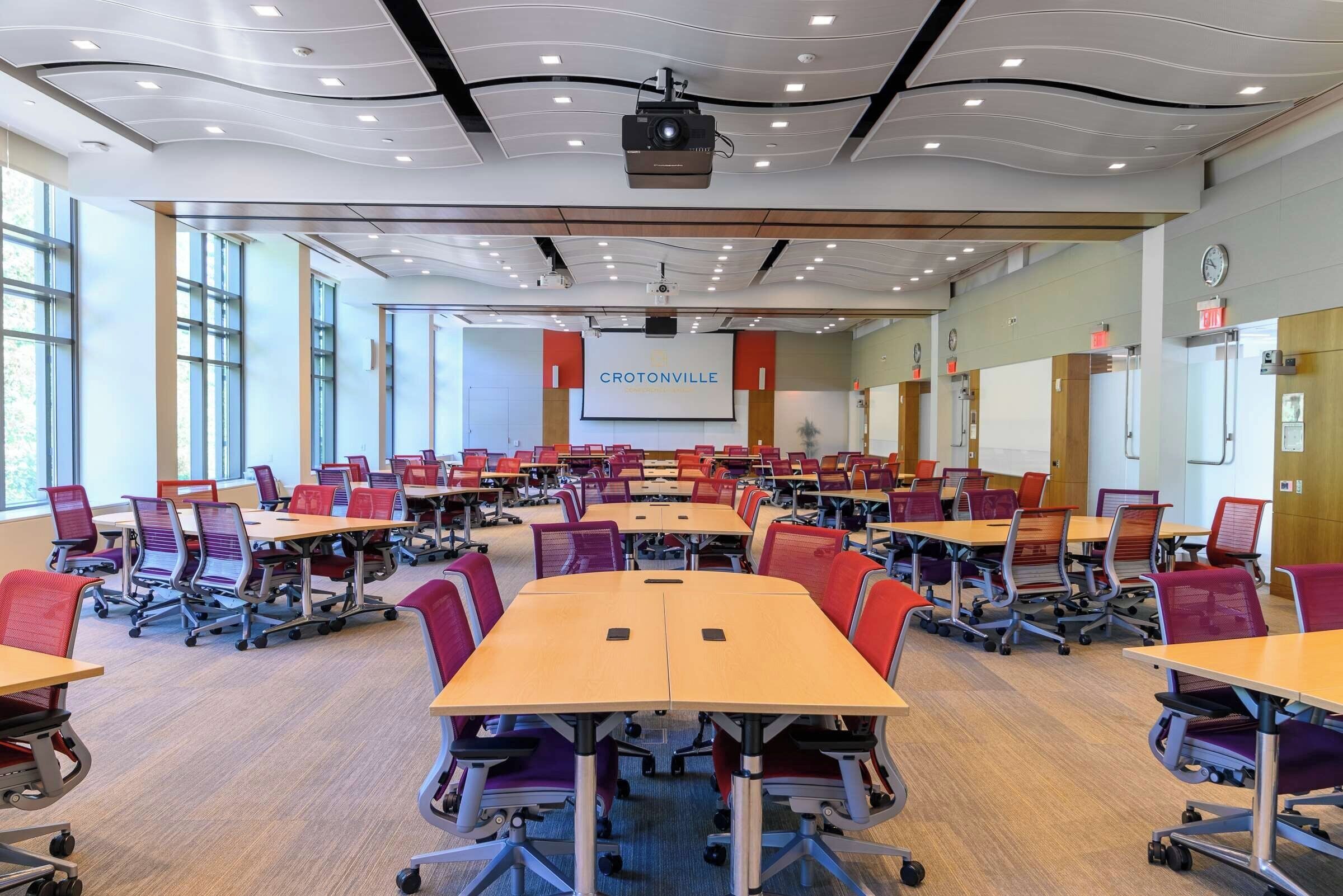 A conference room with multiple tables and chairs, a projector, and a presentation screen.
