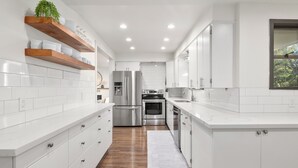 A modern kitchen with white cabinetry, stainless steel appliances, and wooden shelves. - Edmonds Family Home: Walk to Yost Park, Mins to Beach & Downtown (Edmonds)