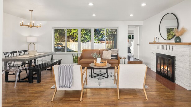 A spacious living room with a fireplace, a dining area with a wooden table and chairs, and a large window offering a view of the outdoors. - Edmonds Family Home: Walk to Yost Park, Mins to Beach & Downtown (Edmonds)