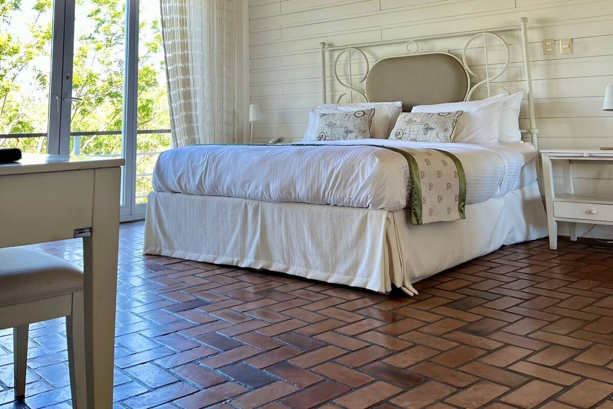 Une chambre à coucher avec un grand lit, une fenêtre avec des rideaux, un plancher en bois et une tête de lit blanche.