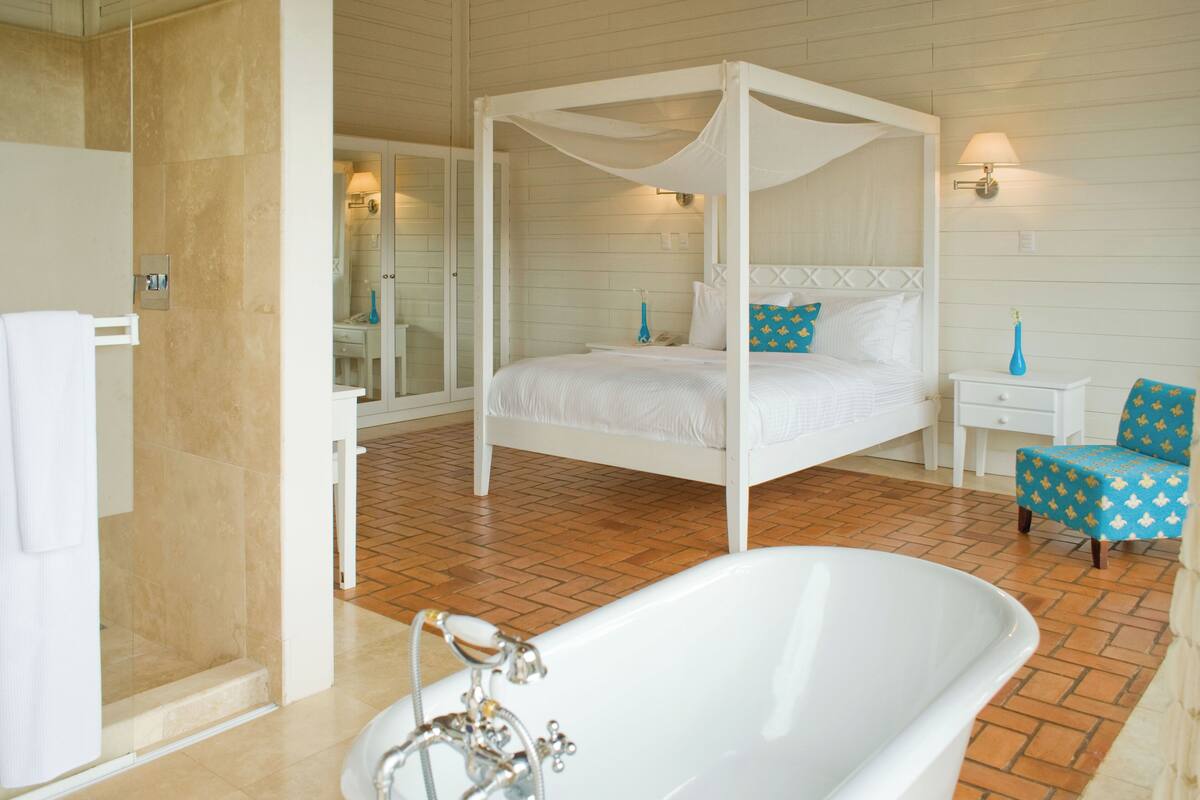 Un lit à baldaquin, une baignoire blanche et une petite table de chevet avec une lampe.