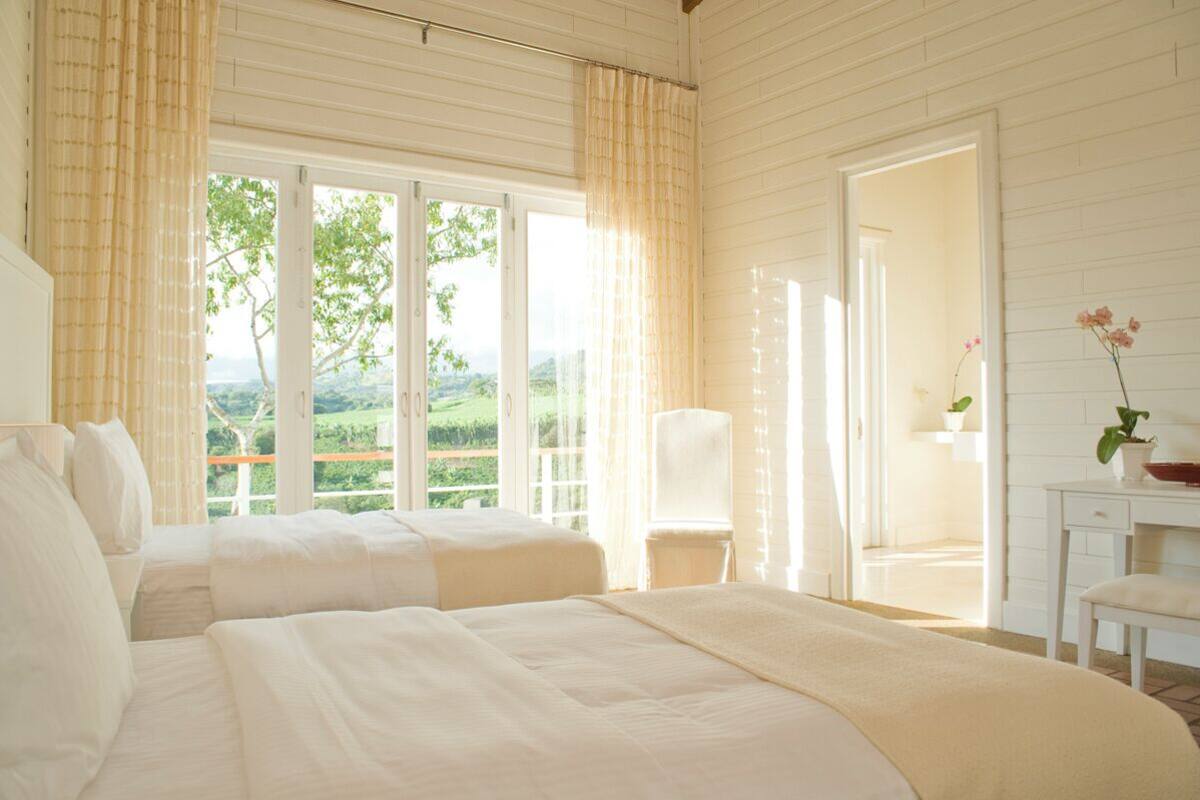 Une chambre avec deux lits, un bureau et une chaise. La fenêtre offre une vue sur la verdure.