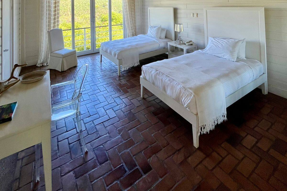 Une chambre d’hôtel avec deux lits, un ventilateur de plafond et une vue sur la verdure par la fenêtre.