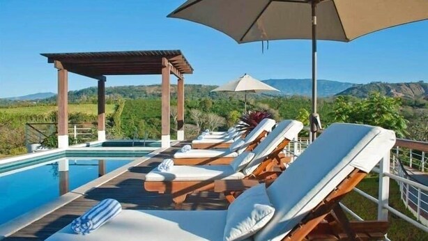 A poolside area with lounge chairs and umbrellas, overlooking a scenic landscape. - Asclepios Wellness & Healing Retreat (Tambor)