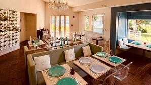 A dining area with a chandelier, wooden tables with green plates, and a green sofa. - Asclepios Wellness & Healing Retreat (Tambor)