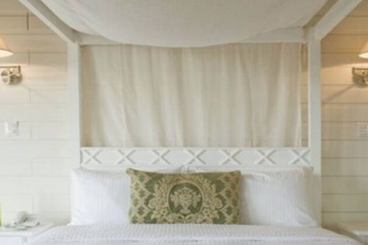 Une chambre à coucher avec un lit à baldaquin, deux lampes de chevet, un téléphone et une bouteille verte posée sur la table de chevet.