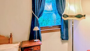 Une chambre à coucher comprenant un lit, une table de chevet, une lampe, une fenêtre avec des rideaux et une vue sur la verdure à l’extérieur.