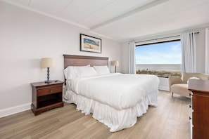 Camera d'albergo con un grande letto, un comodino con una lampada, una sedia e vista sulla spiaggia.