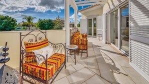 A covered outdoor seating area with a metal bench and a chair, a small round table, and a pergola structure. - Villa Larissa, luxury private villa, pool (Portimão)