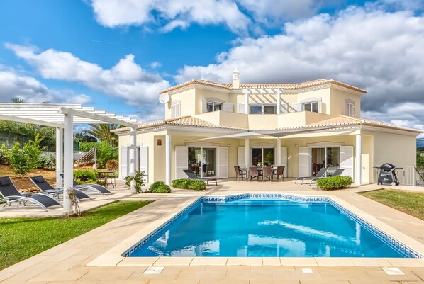 A two-story house with a swimming pool, outdoor seating, and a pergola.