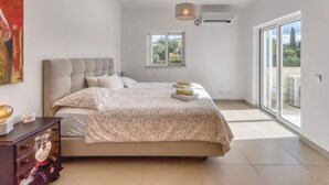 A bedroom with a large bed, a dresser, a ceiling light, a window, and a view of the outdoors. - Villa Larissa, luxury private villa, pool (Portimão)