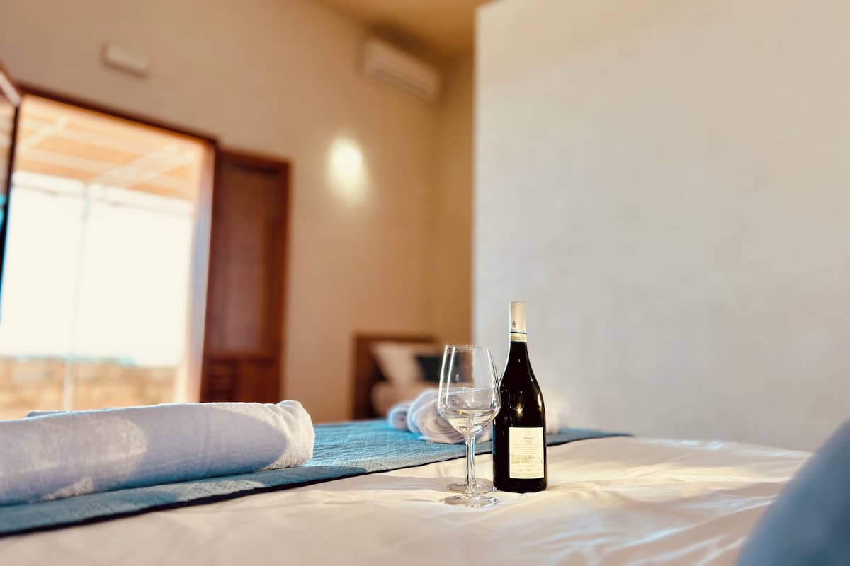 Un letto con una bottiglia di vino e un bicchiere, una coperta blu e una testiera in legno.