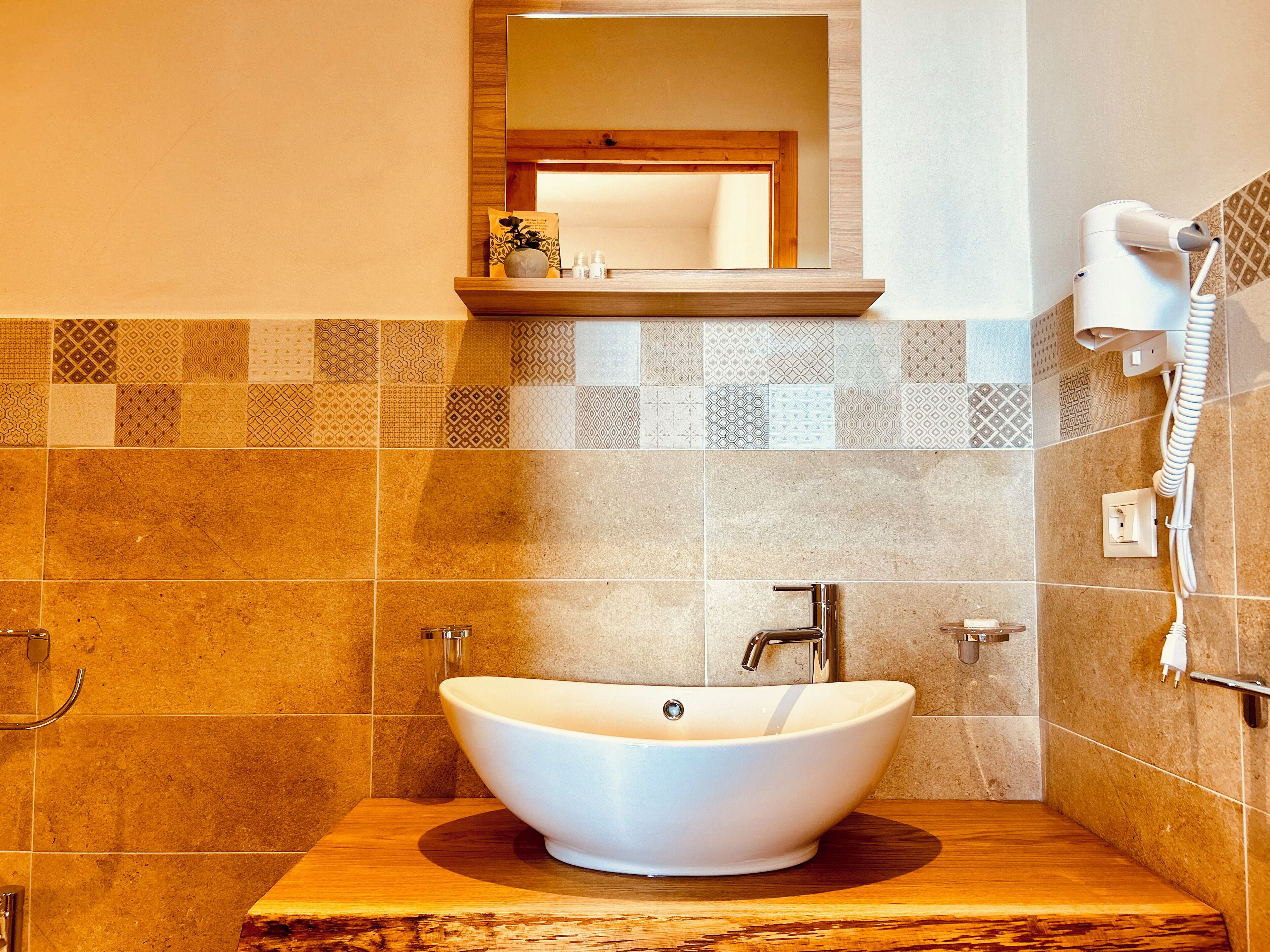 A bathroom with a white vessel sink, a mirror above it, and a hairdryer on the wall.