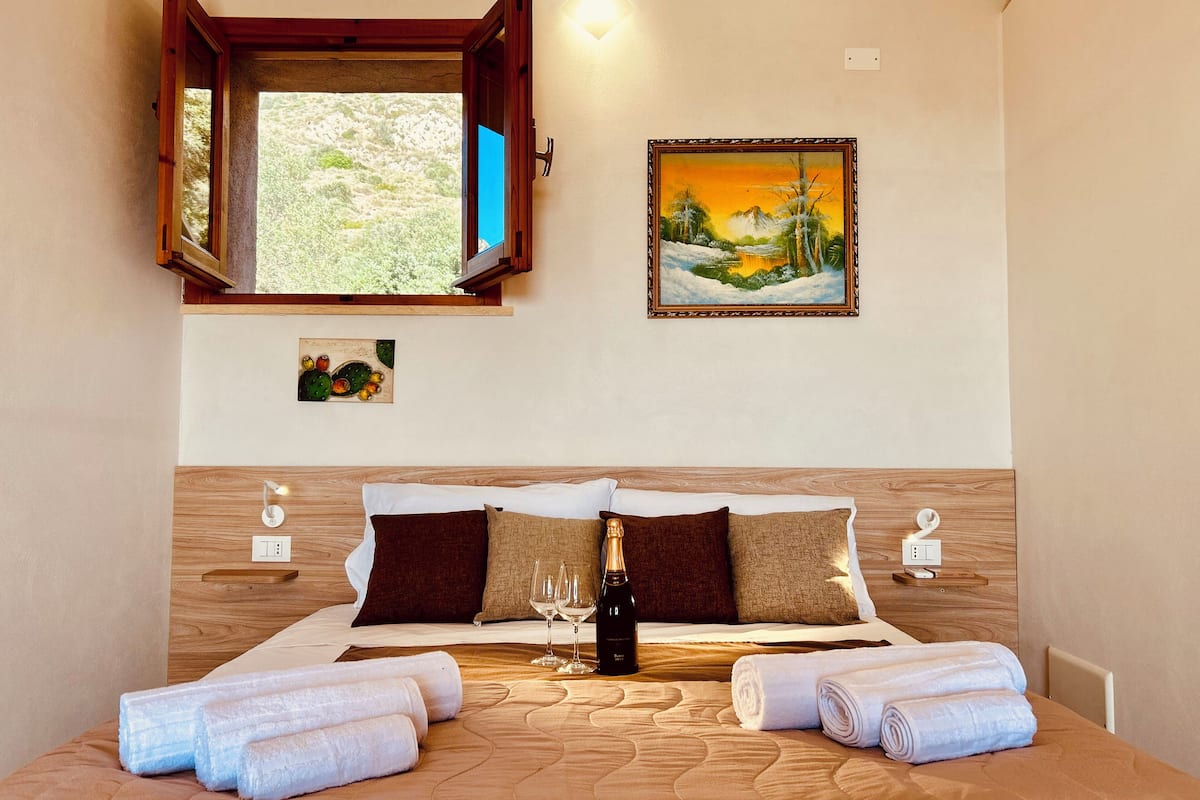 Una camera d'albergo con un letto, un quadro, una finestra e un lampadario a parete.