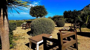A patio area with wooden furniture, a palm tree, and a view of the ocean. - Alencio Panorama Residence (Favignana)