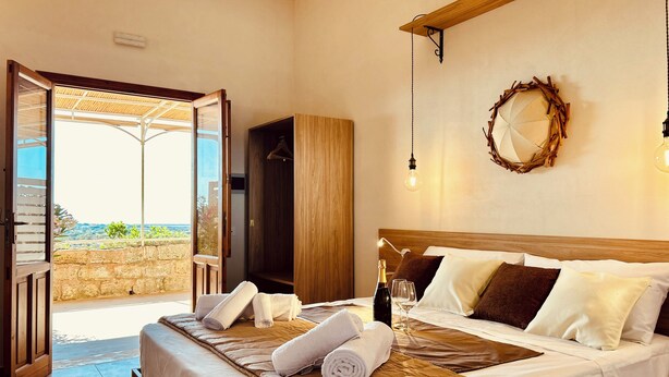 A hotel room with a bed, a wardrobe, a hanging light fixture, and a view of the outdoors. - Alencio Panorama Residence (Favignana)
