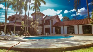 A large house with a swimming pool, surrounded by palm trees and a clear blue sky. - MANSÃO RESIDENCE HOSPEDARIA E EVENTOS (Vassouras)