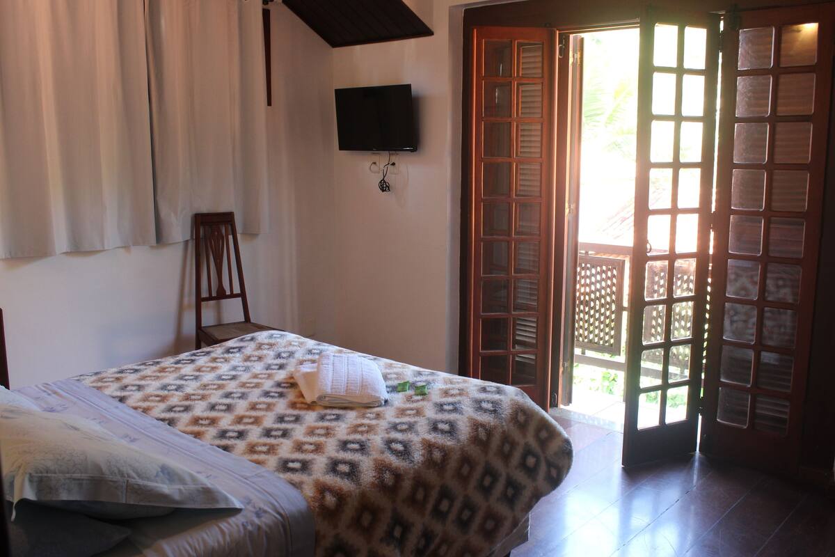 A bedroom with a bed, a television mounted on the wall, a chair, and a door leading outside.