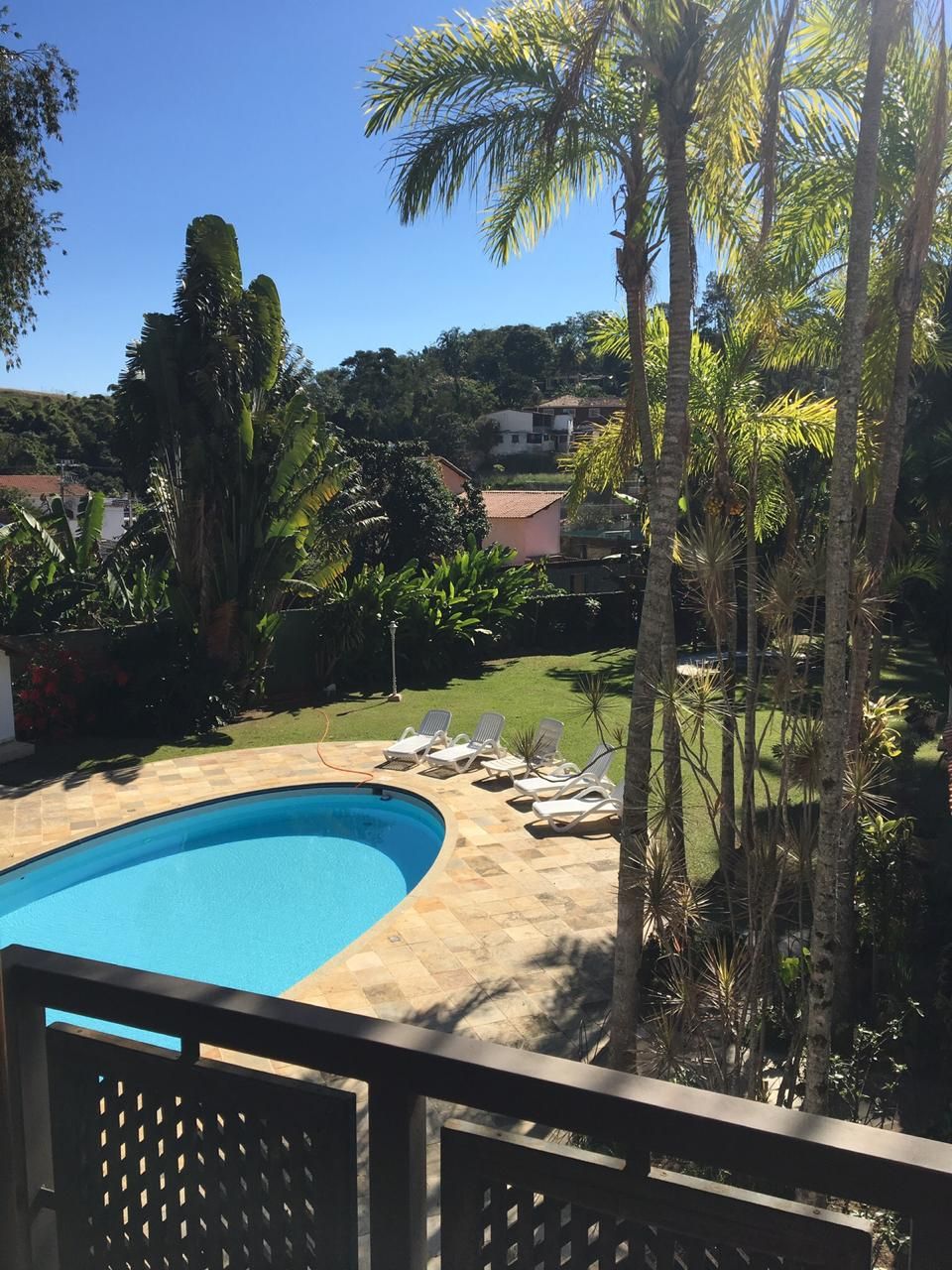 A swimming pool with a tiled deck, surrounded by palm trees and a grassy area with lounge chairs.
