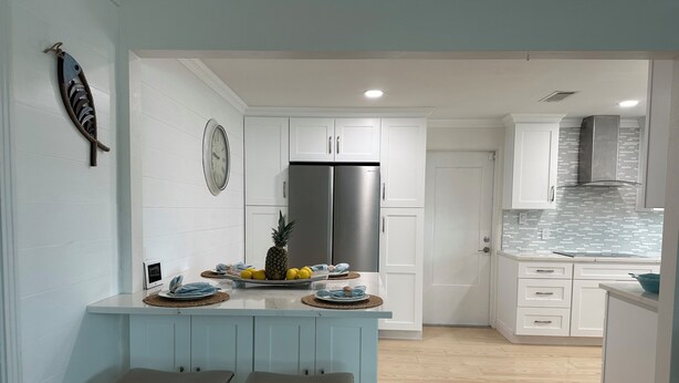 A modern kitchen with white cabinetry, a stainless steel refrigerator, a clock, and a decorative fish wall art piece. - Steps from the Beach, Surrounded by Serenity – Your Coastal Getaway Awaits (Ormond Beach)