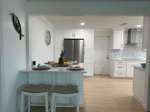 Une cuisine moderne avec des meubles blancs, un réfrigérateur en acier inoxydable, une horloge et un tableau décoratif représentant des poissons.