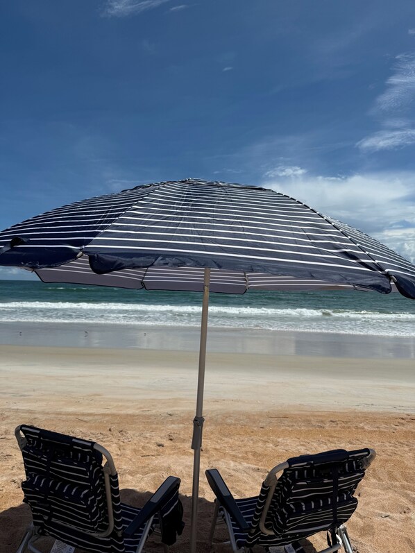 A beach scene with a striped beach umbrella and two beach chairs.
