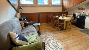 Ein gemütliches Blockhaushaus-Interieur mit Holzbalkendecke, einer Essecke mit Tisch und Stühlen, einer Couch mit Kissen und einer Küchenzeile mit Kühlschrank und Mikrowelle.