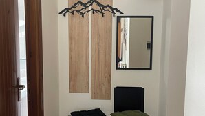 Ein Flur mit einer Holztür, einem schwarzen Stuhl, einem kleinen Tisch mit zwei Kissen, einem Spiegel und einem farbenfrohen Streifen Teppich.