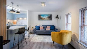 A modern kitchen with a dining area, a sofa, and a yellow armchair. - Sandy Steps - 1 Bedroom Apartment - Tenby (Tenby)