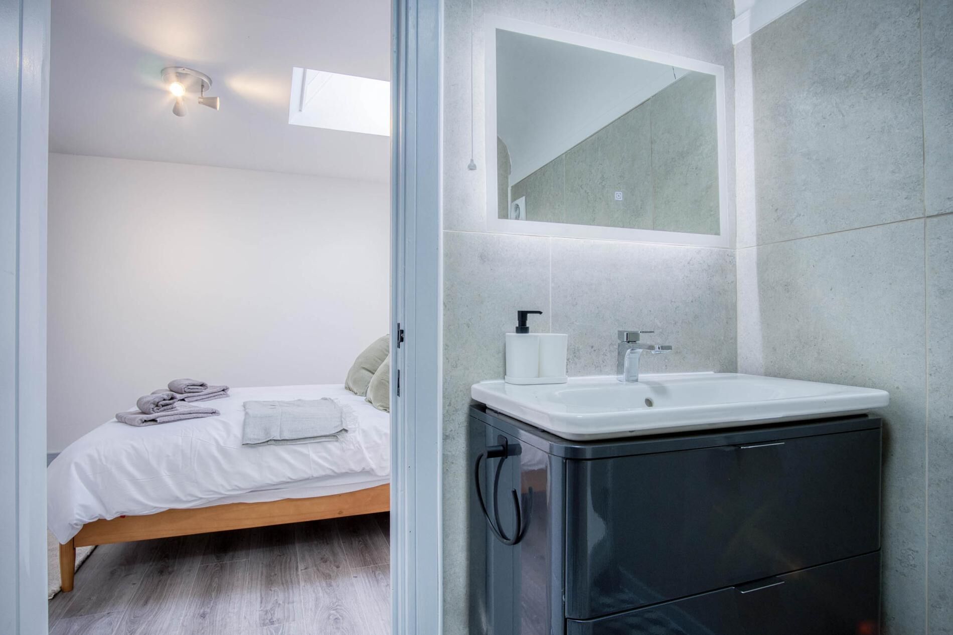 A modern bathroom with a white sink, a mirror, and a bed with neatly folded towels.