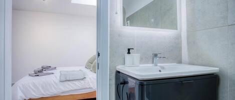A modern bathroom with a white sink, a mirror, and a bed with neatly folded towels.