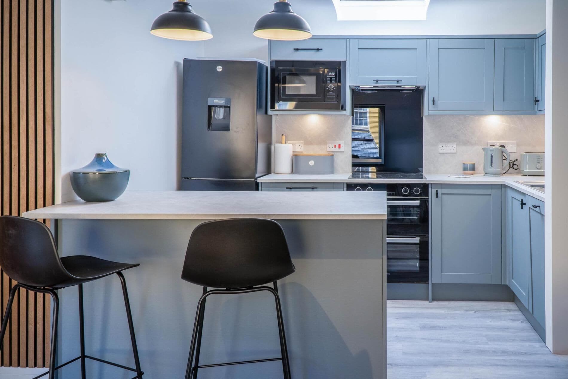 A modern kitchen with a central island, two bar stools, a refrigerator, a microwave, an oven, and a coffee maker.