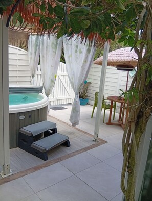 Un bain à remous accessible par des marches, un espace salon couvert et une structure surmontée d’un toit de chaume.