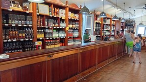 Un bar con estantes de madera llenos de botellas de licores y una barra donde una persona está atendiendo.